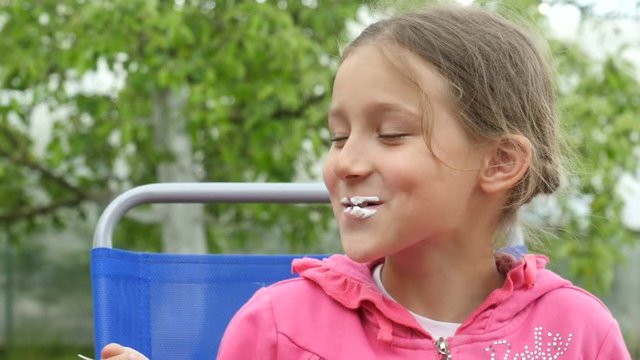 Cute little girl sits and eats ice cream. Child with ice cream. Funny little girl with ice cream. Kid eats ice cream and laughing