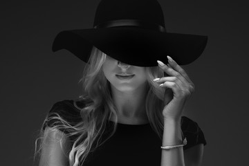 elegant slender girl model in a stylish narrow black dress and a wide hat on a black background....