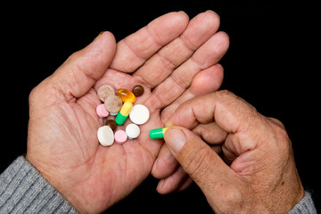 An elderly man holds a lot of colored pills in old hands on a dark background. Painful old age....