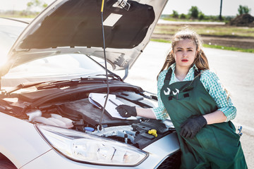 Woman mechanic examining car engine with clipboard
