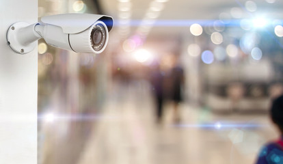 CCTV camera on a wall white. security with supermarket blurred background