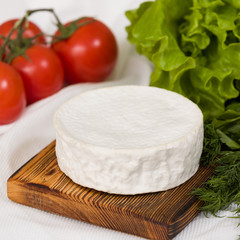 closeup of Camembert cheese on wooden board with tomatoes and green salad on white table background. Serving French homemade soft cheese.