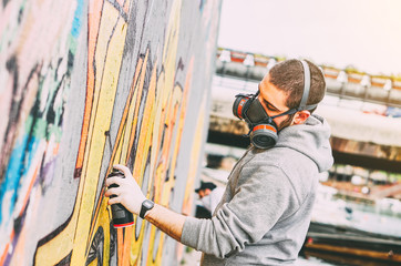 Street artist painting colorful graffiti on a wall under the bridge - Urban man performing with murales - Concept of modern art - Focus on his hand