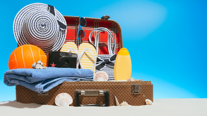 Suitcase with sand and travel supplies