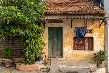 Fototapeta na wymiar A Small Yellow Home with Green Door, Peeling Paint and Faded Door in Bat Trang Pottery Village, Vietnam
