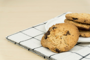the chocolate chip cookies in a white round dish on the cloth at the wooden table.
