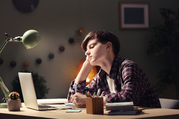 Teenager with laptop doing homework at table in evening