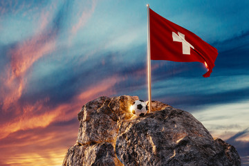 Fussball und wehende Schweizer Fahne auf Bergspitze im wunderschönen Abendlicht