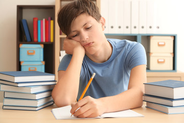 Tired teenager boy doing homework in library