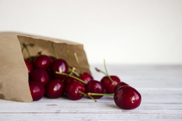 Ripe cherries in a paper kraft pack on a white wooden background, useful fruit from the market.