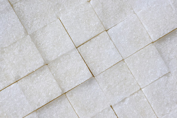 Unhealthy sweet food, obesity and diabetes concept : Top view of pure white refined, bleached sugar cubes / fine granulated sugar sweetener aligned in diagonal view. Abstract texture background.