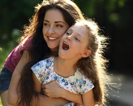 Happy enjoying mother hugging her relaxing smiling kid girl on bright summer background. Closeup portrait