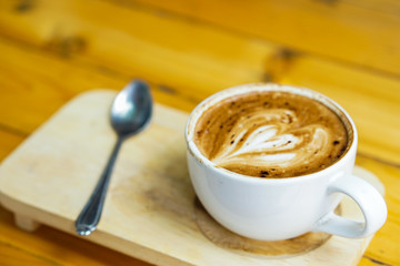 Latte art coffee heart picture placed on wooden tray, on the wooden table background.
