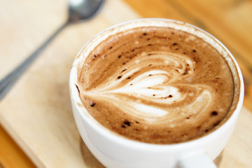 Latte art coffee heart picture placed on wooden tray, on the wooden table background.