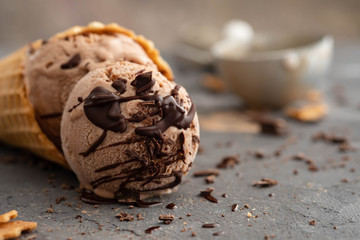 Homemade chocolate ice cream in waffle cones, with a spoon for ice cream, cocoa and pieces of dark chocolate. On a dark gray table. Copy space close view