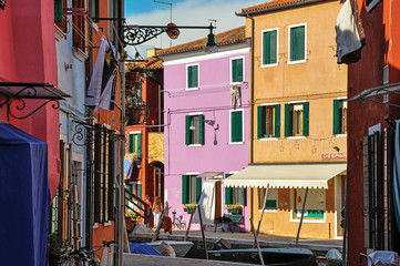 Fototapeta na wymiar View of colorful buildings, people and boats in front of a canal at Burano, a gracious little town full of canals, near Venice. In the Veneto region, northern Italy
