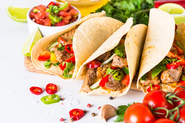 Mexican pork tacos with vegetables and salsa on white.