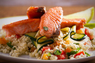 Roasted salmon fish with tomato couscous, zucchini and lime on white plate. horizontal