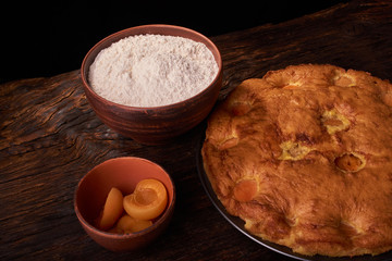 A bowl with flour and apricot cake on a wooden background