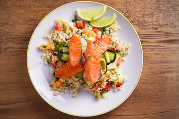 Roasted salmon fish with tomato couscous, zucchini and lime on white plate. overhead, horizontal