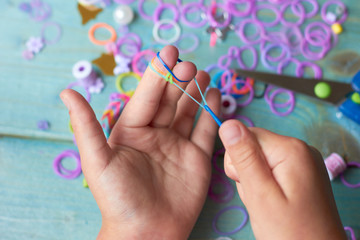 A child is weaving a bracelet of colored rubber bands.