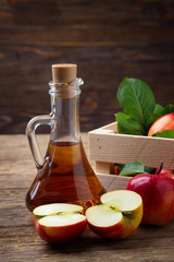Apple cider vinegar and fresh red apple on a wooden background