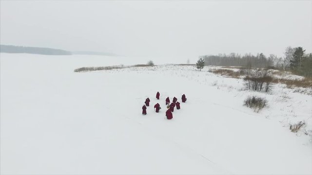 Group of monks in hood robe walking along winter snow trail in forest, aerial view. Footage