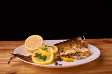 delicious roasted carp fish with lemon slices, spices, and fresh rosemary on white plate, view from above, close-up