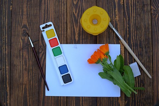 School supplies for drawing lessons on a wooden background. Watercolors, brushes, a glass for water, paper, eraser.  Back to school сoncept. 
