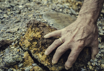 Senior person hand lifting a stone from the ground with the colors of the mineral