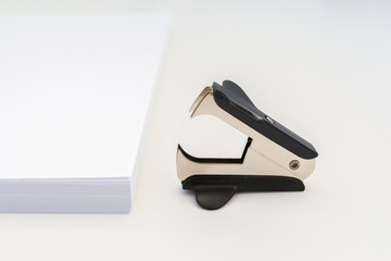 stack of white office paper and a black anti-stapler on a white background, close-up abstract background