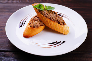 Fresh bruschettas with chicken liver pate on rustic background. Delicious snack, antipasto, appetizing toasts on white plate.