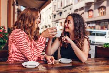 Happy female friends having coffee in outdoor cafe in summer. Women chatting and chilling. Cheers