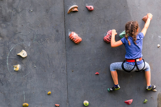 Beautiful young girl climbing to big artificial wall