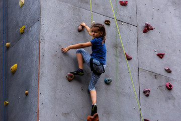 Beautiful young girl climbing to big artificial wall