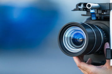 Camera lens attached to a camera and hand focusing close up detailed with smooth blue background and sunset reflections. Concept for videography cinematography vlogging video television movies making 
