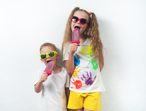 Summer sweets for children: Children boy and girl in sunglasses and colored T-shirts eating pink home ice cream on white background. Portrait.