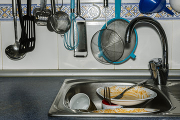 hung kitchenware and a stone mortar with a tile background and sink with dirty food dishes