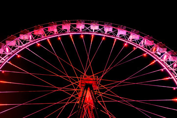 Big ferris wheel with festive red illumination against night sky.