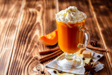 Pumpkin spice latte with whipped cream and cinnamon in glass on rustic wooden background