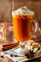 Pumpkin spice latte with whipped cream and cinnamon in glass on rustic wooden background