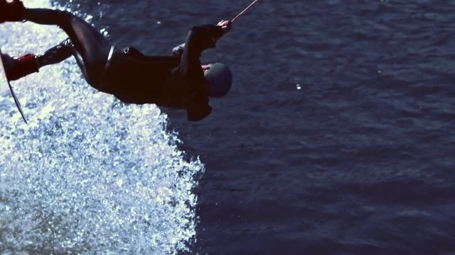 Man riding on wakeboard and falling into water in slow motion. Training in surfing. Athletic man after trick with jump on wakeboard plunging into water. Waterskier in action. Extreme water sports