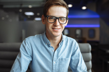 Portrait of a handsome young man, hipster posing with a serious look in glasses, sitting in a cafe, suitable for advertising, text insertion
