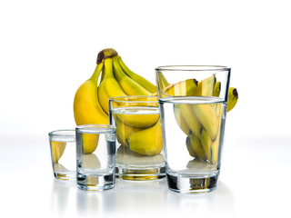Fresh bananas are located behind glasses with water on a white background