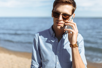 Beautiful stylish business guy with glasses, posing on the beach, hipster talking on the phone, work on vacation, for advertising, text insertion