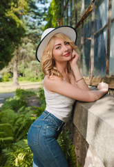 Tender blonde girl wearing hat and stylish outfit posing near the greenhouse