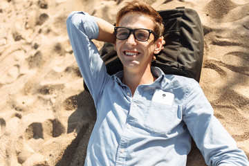 Young guy with glasses, posing, lying on the beach on the sand, work on vacation, suitable for advertising