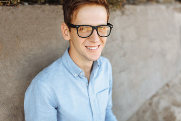 Young guy with glasses, working on his laptop on the beach against the gray wall, at sunset, working on vacation, suitable for advertising, text insertion