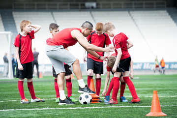 Full length portrait of junior football team practicing in stadium, focus on coach giving...