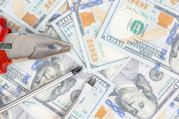 Tools lying over 100 dollars banknotes background. Pliers and screwdriver against US money. Correction, fixing and improvement of budget concept. Copyspace